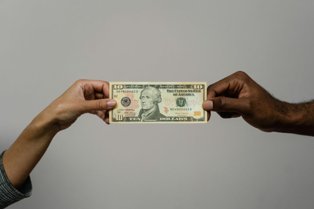 Close-up of two hands exchanging a ten dollar bill, symbolizing financial transaction or exchange.